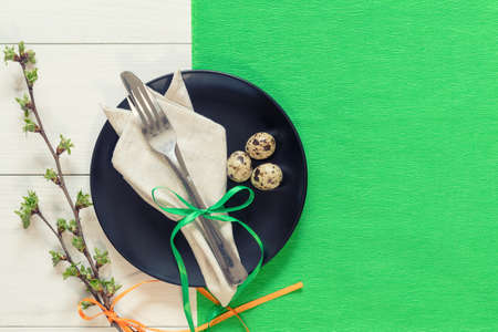 Easter table setting with spring flowers and cutlery. Rustic green table cloth on white wood background. Holidays background with copy space.の写真素材