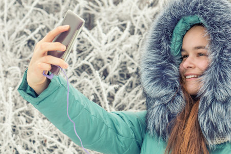 Pretty girl doing a selfie with her smart phone. Beautiful young woman. Outdoor winter portrait....