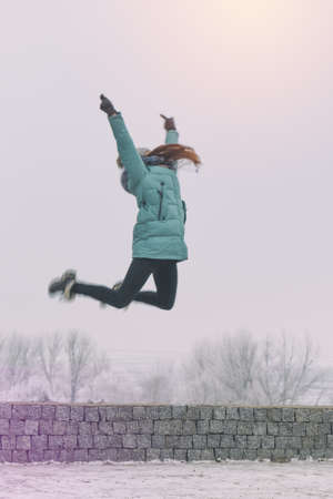 Young girl is jumping in winter snow park. Toned and processing photoの写真素材