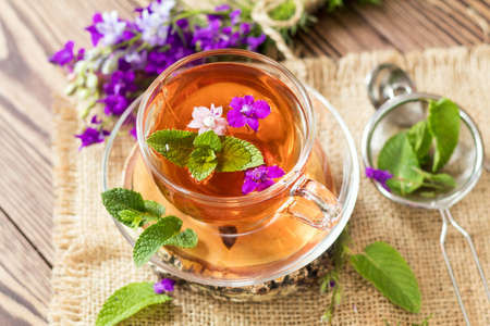 Glass cup of summer herbal tea with fresh mint and field larkspur. Wooden table. Shallow depth of field.の写真素材