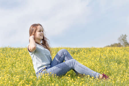 Young girl teenager on a lawn field with yellow flowers. Long chestnut hair. Sunshine, springtime, blue sky. Coloring and processing photos with soft selective focus. Shallow depth of field.の写真素材