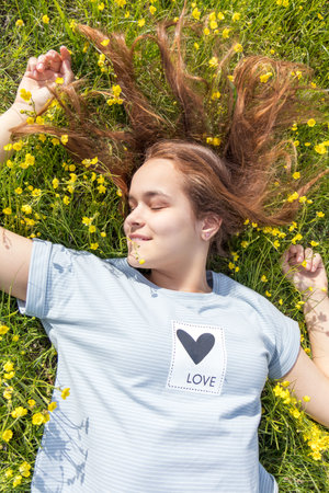 Young girl teenager on a lawn field with yellow flowers. Long chestnut hair. Sunshine, springtime, blue sky. Coloring and processing photos with soft selective focus. Shallow depth of field.の写真素材