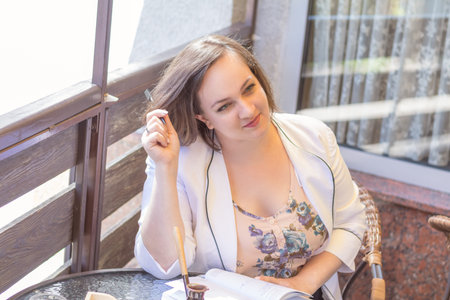 Young business lady working in the street cafe. Coffee and cakes on the table. Sunny day. Coloring and processing photos. Shallow depth of field.の写真素材
