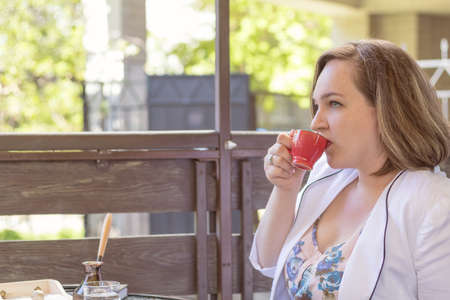 Young business lady drinking coffee in the street cafe. Coffee and cakes on the table. Sunny day. Coloring and processing photos. Shallow depth of field.の写真素材