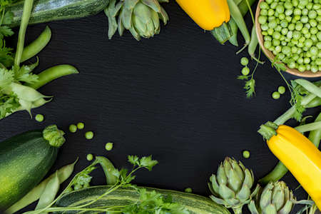 Fresh organic green vegetables on black stone floor with copy space. Green and yellow vegetables background. Healthy eating background. Vegetarian food, organic food.の写真素材