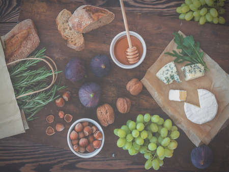 Sandwiches with ricotta, fresh figs, prosciutto, rosemary and blue cheese, walnuts and honey on rustic wooden board over black backdrop, top view. Delicious fruity breakfast. Tonedの写真素材