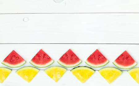 Red and yellow watermelon slices on wooden sticks on a white wooden background. Flat lay, top view, copy spaceの写真素材