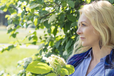 Pretty romantic blonde woman in the city park on a spring sunny day. Spring blossom and green leaves are at the background. Peaceful, quiet romantic atmosphereの写真素材