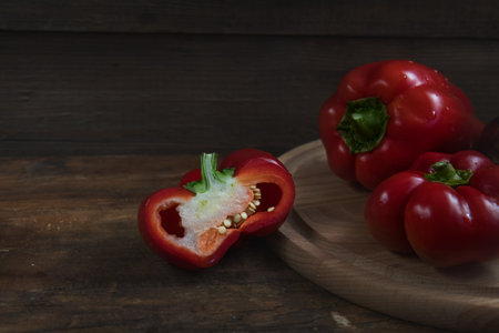 Red and purple sweet pepper on a round wooden cutting board on a dark wooden background. Copy space
