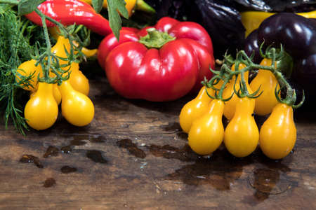 Red and purple sweet pepper and yellow tomatoes on a dark wooden backgroundの写真素材
