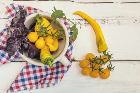 Yellow hot pepper and yellow tomatoes with purple basil in a ceramic white pot on a checkered cloth. Top view. Copy spaceの写真素材