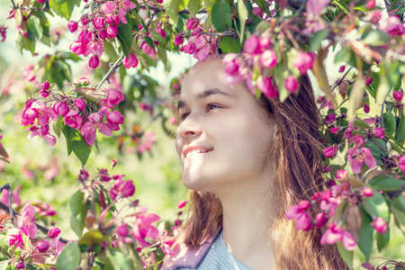 Cute romantic young girl with closed eyes smelling the aroma of apple blossom in an apple orchard in the springtime. Sunny spring day. Peaceful, quiet romantic atmosphereの写真素材