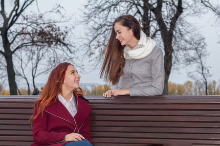 Female teenagers listening to music on smartphone at the bench in an autumn city parkの写真素材