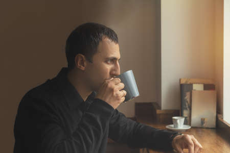 Young man in casual clothes drinks coffee while sitting in a cafe. Man drink coffee in cafe. Cozy atmosphere. Coloring and processing photo.の写真素材