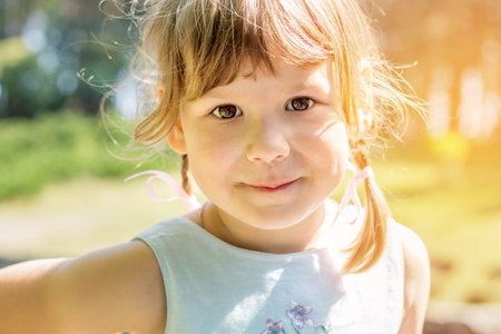 Cute little girl plaing in the city park on a summer sunny day. Portrait little girl close up, big...