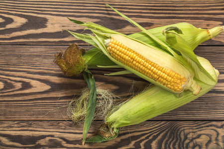 Fresh corn on cobs on rustic wooden table, top view. Dark wooden background freshly harvested...