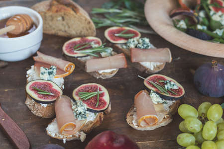 Easy diet salad with arugula, figs and blue cheese on a brown wooden surface. Sandwiches with ricotta, fresh figs, prosciutto, rosemary and blue cheese. Delicious fruity breakfast, top view. Toned.の写真素材