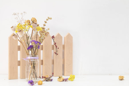 Dried flowers and poppy heads on a stem in a glass jar. Wooden decoration. White wooden table, white...