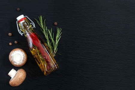 Rosemary bunch, mushrooms, olive oil with pepper and spices and fragrant pepper on black stone surface. Top view, copy space.の写真素材
