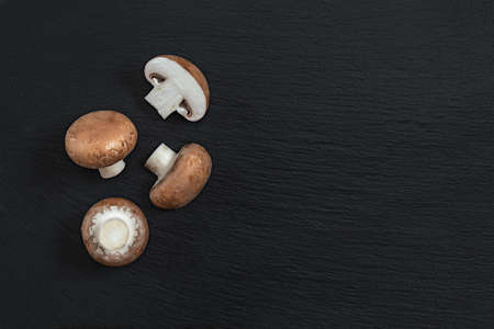 Mushrooms on black stone surface. Top view, copy space. Fresh raw champignon with a brown cap on dark background.の写真素材