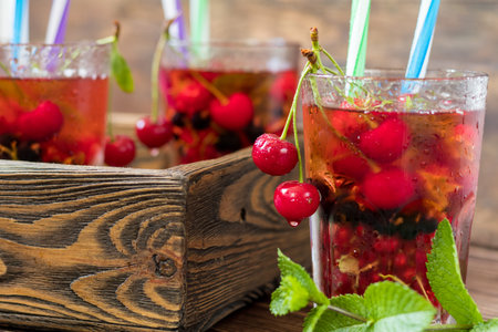 Glasses of refreshing drink flavored with fresh fruit and decorated with cherries covered with dew drops. Wooden backgroundの写真素材