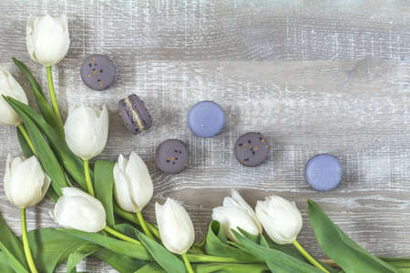 Many white tulips and gray macaroons on light wooden surface. Beautiful romantic background with copy space. Wedding, birthday, easter, mother day, valentine day composition.の写真素材
