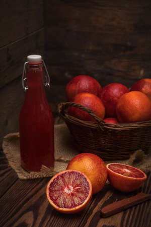 Blood orange fruit in a wicker basket and bottle juice on dark wooden table. Dark rustic style.の写真素材