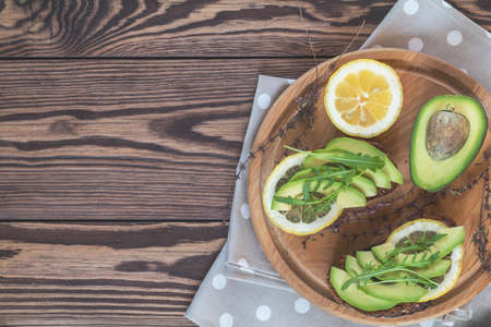 Healthy delicious nutritious breakfast. Rye bread with avokado and limon, fresh arugula on round board. Dark wooden table, top view, copy space.の写真素材