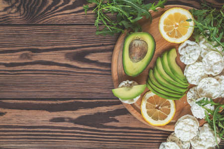 Healthy delicious nutritious breakfast. Rye bread with avokado and limon, fresh arugula, nutritious cereal breads on round board. Dark wooden table, top view, copy space.の写真素材