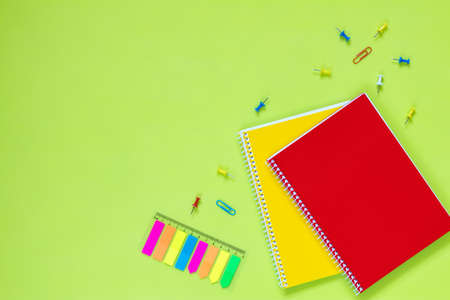 Beautiful office stationery flat lay with ruled red and yellow notebooks, stationery and office supplies and paper clip on the bright desk with green background.の写真素材