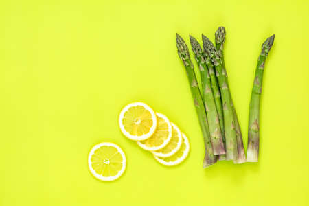 Beautiful food art background. Asparagus sprouts and sliced lemon on bright green surface.の写真素材