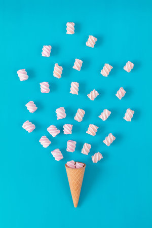 Waffle cone with marshmallow bouquet on blue surface. Flat lay, top view sweet food background.