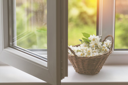 Cozy spring summer home concept. Jasmine flowers blooming in wicker basket on windowsill. Toned and...