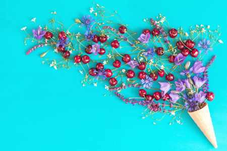 Waffle cone with red cherries, cornflower, blue bells and white flowers blossom bouquets on blue...