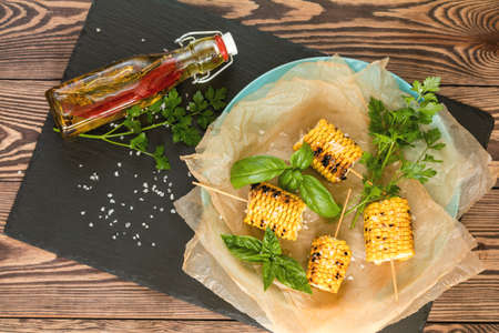 Corn baked in olive oil, with pepper, salt and basil on blue dish on a black stone on dark wooden surface. Vegetarian, vegan menuの写真素材