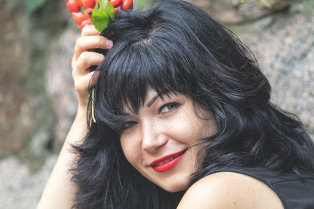 Red rose hips in women's hands. Sexy beautiful pretty brunette with red lipstick. Selective focus,...
