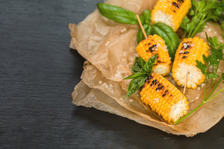 Corn baked in olive oil, with pepper, salt and basil on blue dish on a black stone surface....