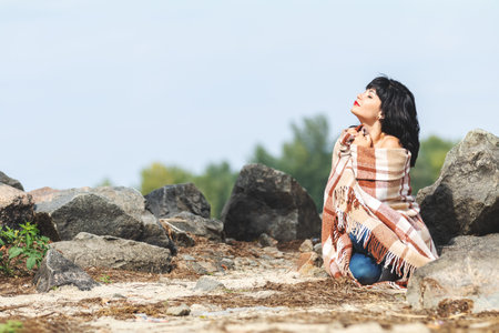 Cute happy beautiful sexy brunette female girl resting sitting on the stone near river, wrapped in a...