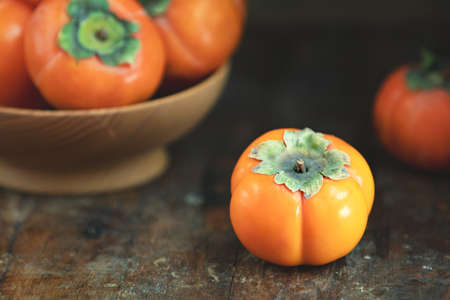 Autumn harvest Persimmon fruits in bowl on a wooden table background. Copy space. Dark rustic style. Natural remedyの写真素材
