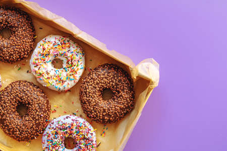 Delicious glazed donuts in box on violet surface. Flat lay minimalist food art background. Top view.の写真素材
