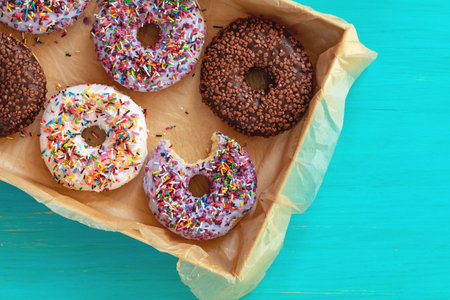 Delicious glazed donuts in box on turquoise blue surface. Flat lay minimalist food art background. Top view.の写真素材