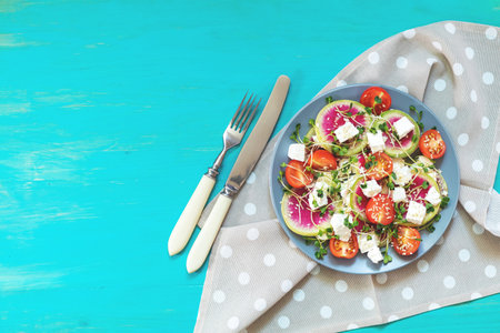 Healthy delicious tasty salad with tomatoes, radishes, cheeses, sprouts and sesame in plate on turquoise wooden background, top view, copy space.の写真素材