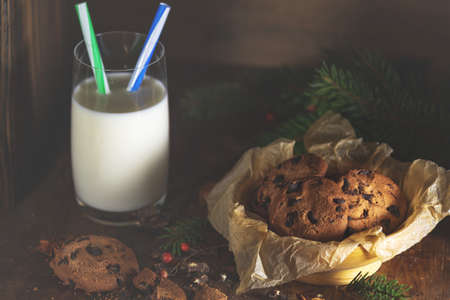 Christmas and New Year composition with delicious chocolate cookies and glass of milk, spruce branches and pine cones on dark wooden background.の写真素材