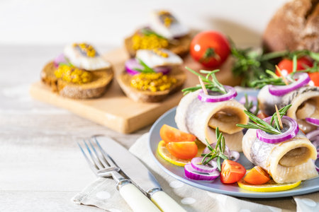 Delicious rolled herring fillet with red onion, cherry tomatoes, lemon and rosemary. Close up,...