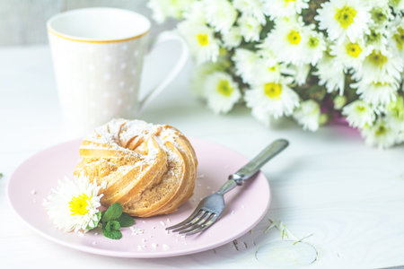 Delicious cake with coconut chips on pink  plate on white table, autumn white chrysanthemum and cup...