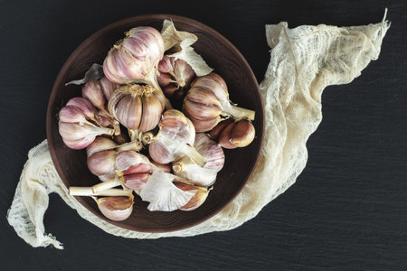 Fresh garlic heads, cloves set in plate on a black stone surface, top view, copy space, free space...