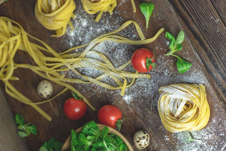 Raw homemade Italian typical pasta linguine noodles, quail eggs, green lettuce, tomatoes and flour on dark wooden table. Shallow depth of the field, close up, copy space.の写真素材