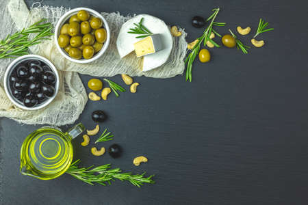 Set of cheese camembert, black and green olives, quail eggs on plates, olive oil and rosemary, cashew nuts, on black stone background background. Top view, copy space.の写真素材