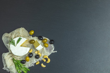 Set of cheese camembert, black and green olives, quail eggs, rosemary, cashew nuts, on black stone background background. Top view, copy space.の写真素材