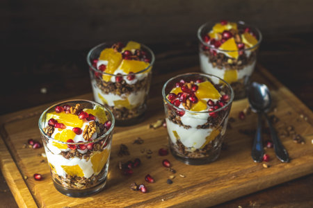 Greek yogurt parfait with granola, orange and pomegranate berries for healthy breakfast on dark...